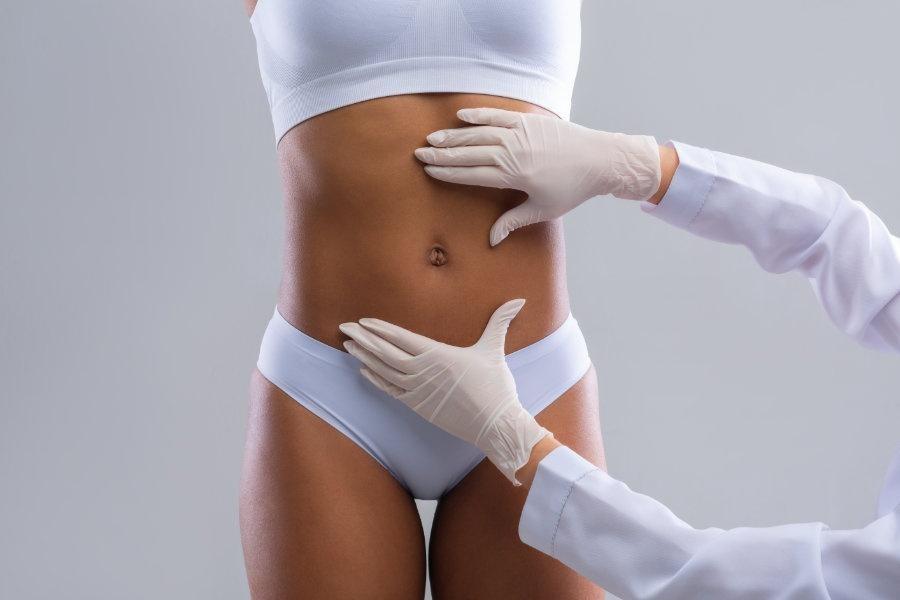 Cropped of plastic surgeon hands checking afro woman belly before beauty procedure, liposuction concept